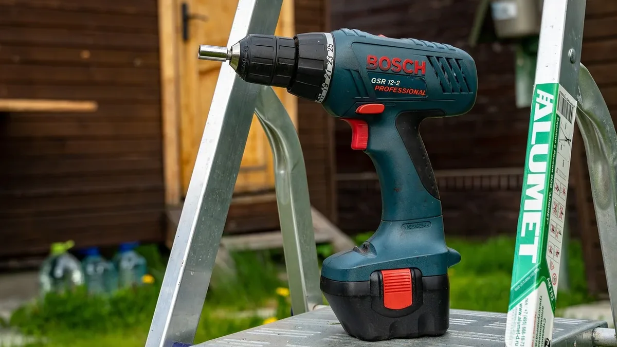 A Bosch drill on a metal step ladder in front of a wooden building.
